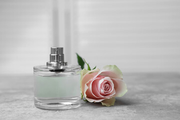 Bottle of perfume and rose on grey table indoors, space for text