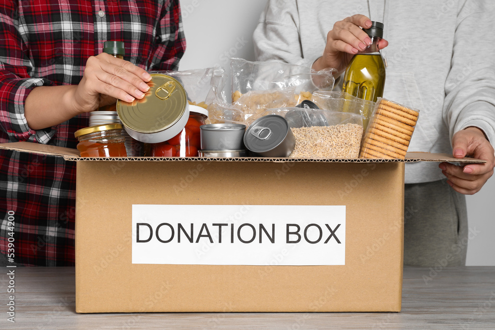 Wall mural women taking food out from donation box at wooden table, closeup