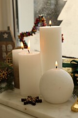 Beautiful burning candles with Christmas decor on windowsill indoors