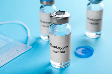 Monkeypox vaccine in glass vials and medical mask on light blue background