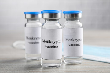 Monkeypox vaccine in glass vials and medical mask on wooden table