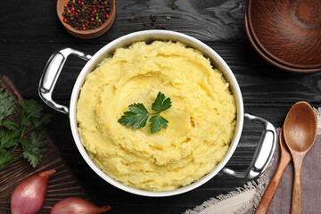 Pot of tasty mashed potatoes with parsley on black wooden table, flat lay