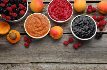 Different puree in bowls and fresh fruits on wooden table, flat lay. Space for text