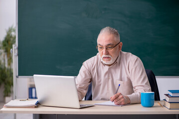 Old male teacher in front of blackboard