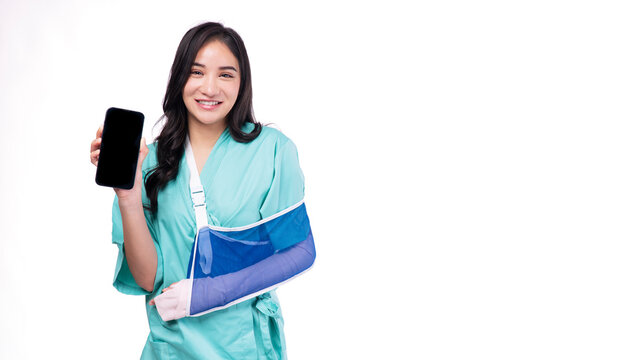 Injured asian woman painful accident broken hand soft splint arm showing blank mobile phone standing on white background. Smile young girl hold smartphone over isolated.Insurance accident health care.
