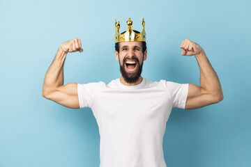 Portrait of excited strong confident man with beard wearing white T-shirt and gold crown, showing...