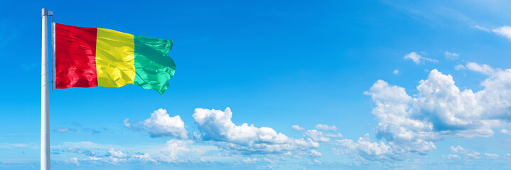 Guinea flag waving on a blue sky in beautiful clouds - Horizontal banner
