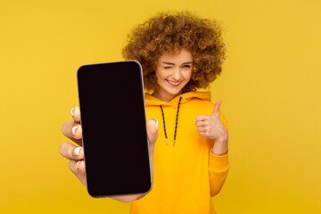 Portrait of joyful pleased woman with Afro hairstyle wearing casual style hoodie showing thumb up...