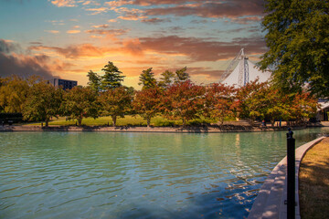 Fototapeta na wymiar a stunning autumn landscape at World's Fair Park with a pool with blue water surrounded by red and yellow autumn trees and lush green trees and plants with powerful clouds at sunset in Knoxville