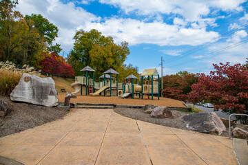 a brown and white jungle gym on a playground surrounded by red and yellow autumn trees and lush...