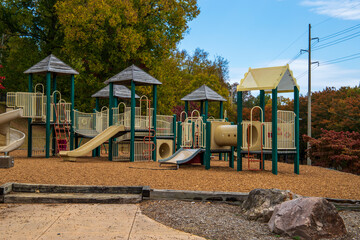 a brown and white jungle gym on a playground surrounded by red and yellow autumn trees and lush green trees with blue sky and clouds at Alex Haley Heritage Square in Knoxville Tennessee USA - obrazy, fototapety, plakaty