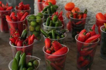 Many plastic cups with fresh chilli peppers on grey counter at market, closeup