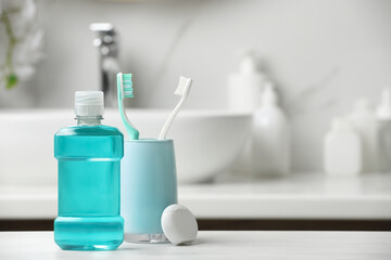 Mouthwash, toothbrushes and dental floss on white countertop in bathroom. Space for text