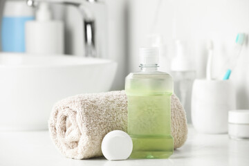 Fototapeta na wymiar Mouthwash, towel and dental floss on white countertop in bathroom
