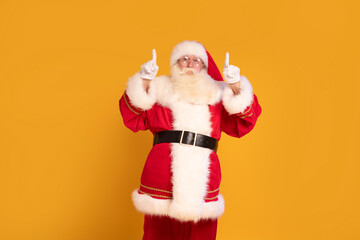 Real Santa Claus showing empty advertisement place on yellow studio background with copy space....