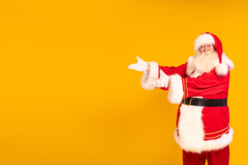 Fototapeta na wymiar Santa Claus showing empty advertisement place on yellow studio background with copy space. Christmas is coming. Time for xmas gifts.