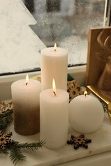 Beautiful burning candles with Christmas decor on windowsill indoors