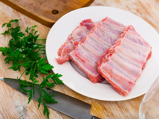 Raw pork ribs served on white plate with herbs, ready-to-cook