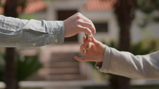 Close up Asian American female hand passing key male outdoors sunlight. Woman handing keys new house man customer. Buying dwelling. Selling home. Real-estate agent job. Handing over keys young couple.