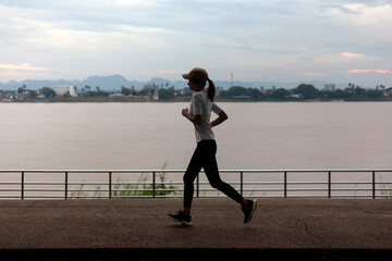 Woman in exercise clothes jogging in the morning along the Mekong River bank in Nakhon Phanom province with beautiful views of the Mekong River and Laos mountains.