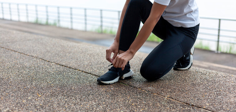 A woman wearing exercise clothes is tying her shoelaces in preparation for a morning jog.