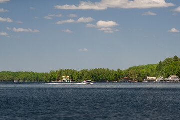 Fototapeta na wymiar Speeding boat on Lake Joseph in Muskoka, Ontario. Cottagese nestled between green trees are visible