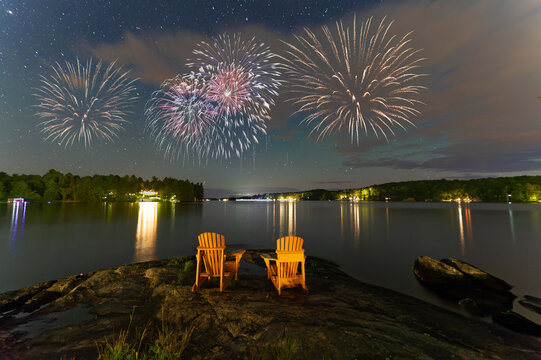 Canada Day fireworks over two Adirondack chairs  in Muskoka, Ontario Canada. The pyrotechnics are illuminating a sky full of stars
