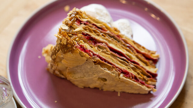Trozo de torta de hojarasca, con interior de manjar y mermelada de frambuesa. Cubierto por una capa de crema merengue blanco. Sobre un plato de cer&aacute;mica color morado