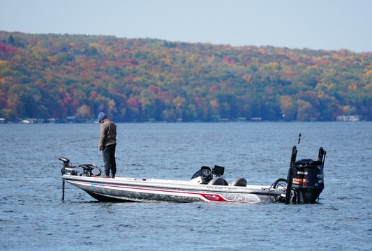 Cayuga Lake, New York, U.S - October 15, 2022 - A fisherman on the boat with the background of fall foliage