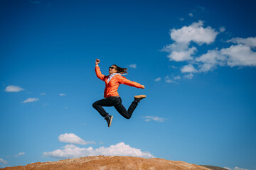 Athletic woman jumping against the blue sky. Happy young girl enjoying active vacation. Travel and fun concept.