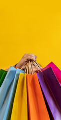 Close-up of a woman's hand holding colorful shopping bags over yellow background. Copy space....