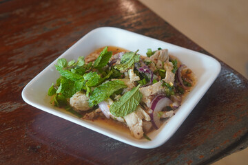 Grilled Pork Neck Nam Tok on square white plastic dish on wooden table background, food, nature, health, copy space