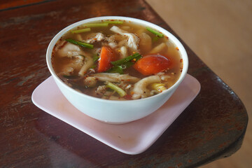   Spicy soup with cartilage in a white plastic bowl on a pink plastic square plate, on wooden table, nature, food, vegetables