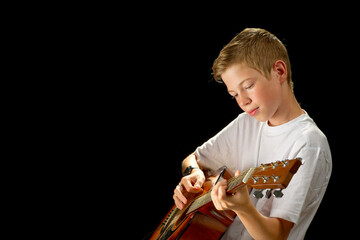 Happy boy playing on acoustic guitar. Teenager boy with classic wooden guitar. boy learning to play guitar on black background. Music education and extracurricular lessons.