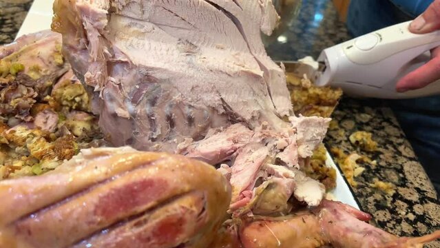 Using an electric knife, they cut a festive turkey for Thanksgiving or New Year or Christmas White brisket meat is laid out on a snow-white plate Delicious delicacies for holiday man slicing