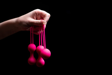 Woman's hand holds pink Kegel balls / Ben Wa balls on a black isolated background. Vaginal balls in...
