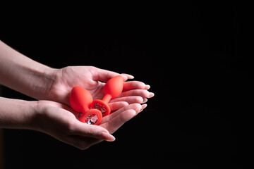 Two red anal plugs in female hands on a black isolated background. Sex toys for ass. Copy space for...