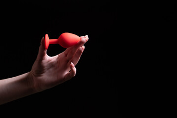Red anal plug in female hands on a black isolated background. Sex toys for ass. Copy space for text - obrazy, fototapety, plakaty