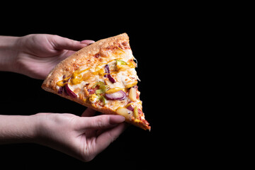 Piece of pizza with chicken, pineapple, vegetables, curry sauce in female hands on a black isolated...