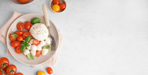 Plate with delicious mozzarella cheese, basil and tomatoes on light background with space for text, top view