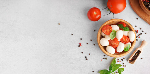 Wooden bowl with tasty mozzarella cheese, tomatoes and spices on light background with space for text, top view