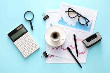 Business charts, cup of coffee and stationery on blue background