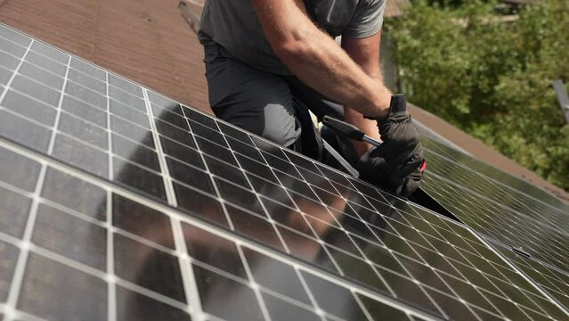 Technician attaching solar panel to roof of customers house, sustainable energy