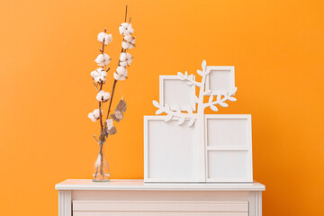Family tree with photo frames, vase and cotton flowers on shelf near orange wall