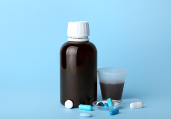 Bottle and cup of cough syrup with pills on blue background