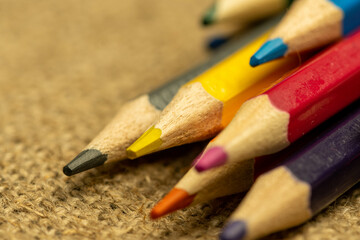 Several colored pencils of different colors on a background of coarse burlap. Close-up, selective focus.
