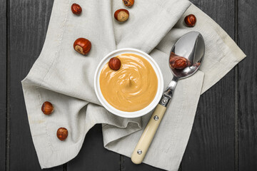 Bowl of tasty hazelnut butter and nuts on dark wooden background