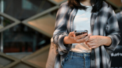 A hipster young Asian female in a flannel shirt uses her smartphone in the shopping mall.