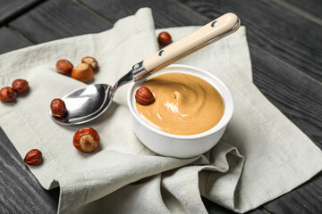 Bowl of tasty hazelnut butter and nuts on dark wooden background, closeup