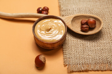 Bowl of tasty nut butter and hazelnuts on color background